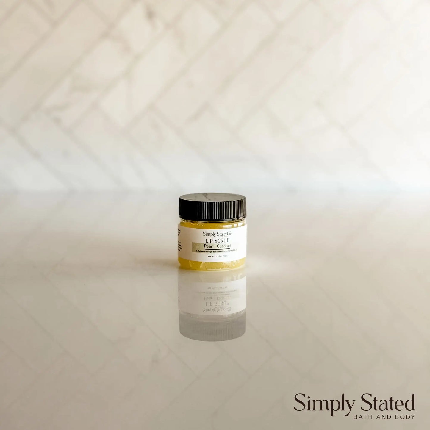 Simply Stated Bath and Body Peach Cobbler Lip Scrub jar standing on marble surface against tiled backdrop.