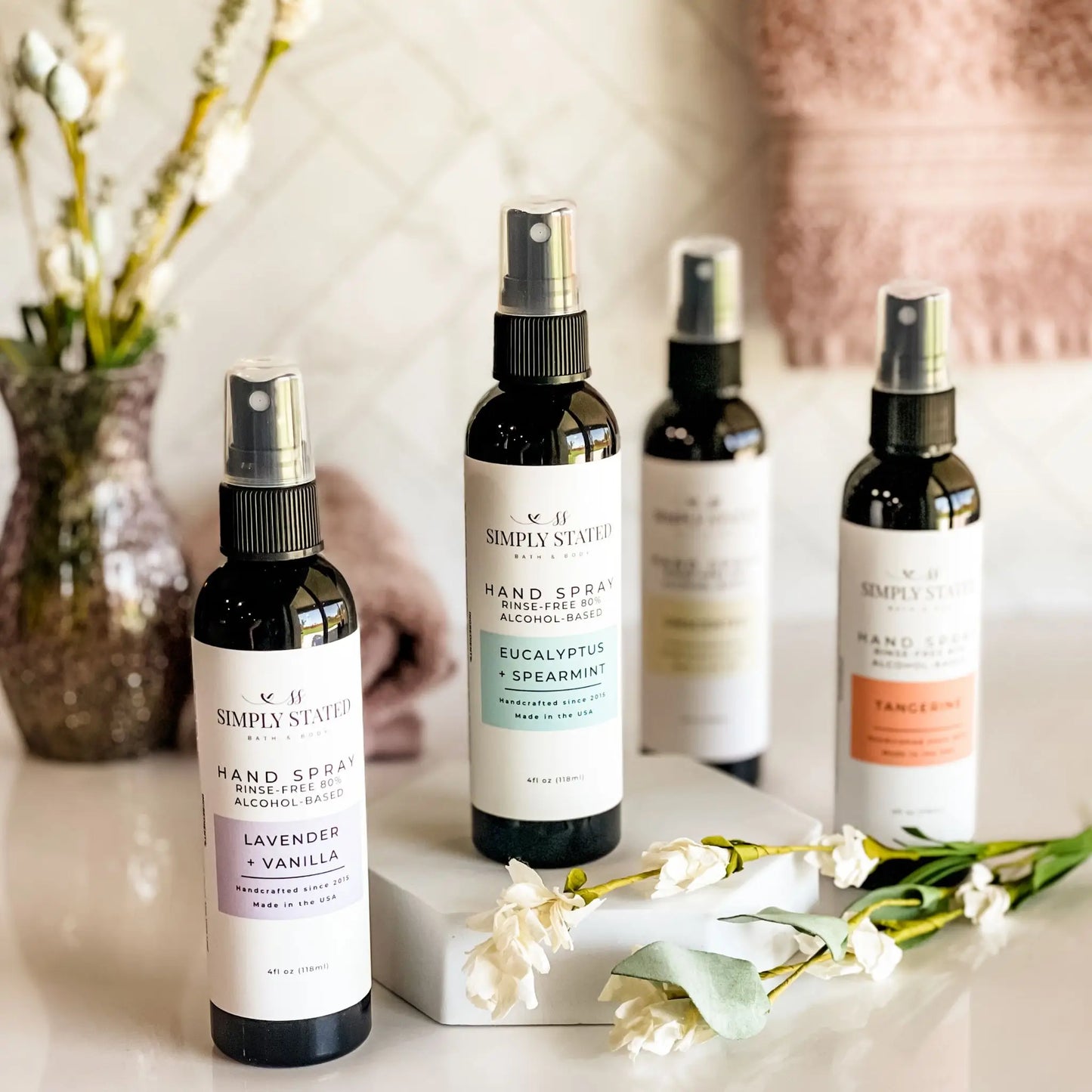 Collection of Simply Stated hand spray bottles on a surface with flowers in the background