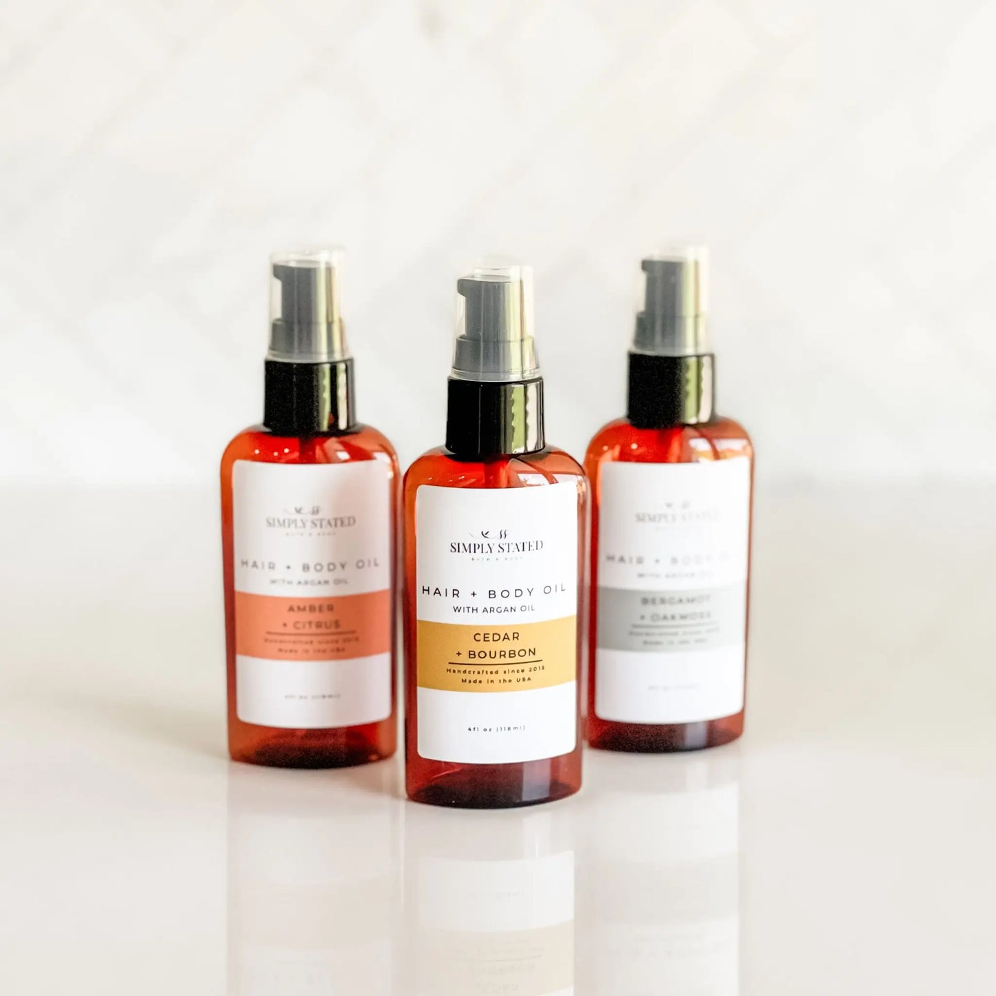Simply Stated Bath & Body Hair + Body Oil in Cedar + Bourbon, Amber + Citrus, and Bergamot + Oakmoss, three amber bottles