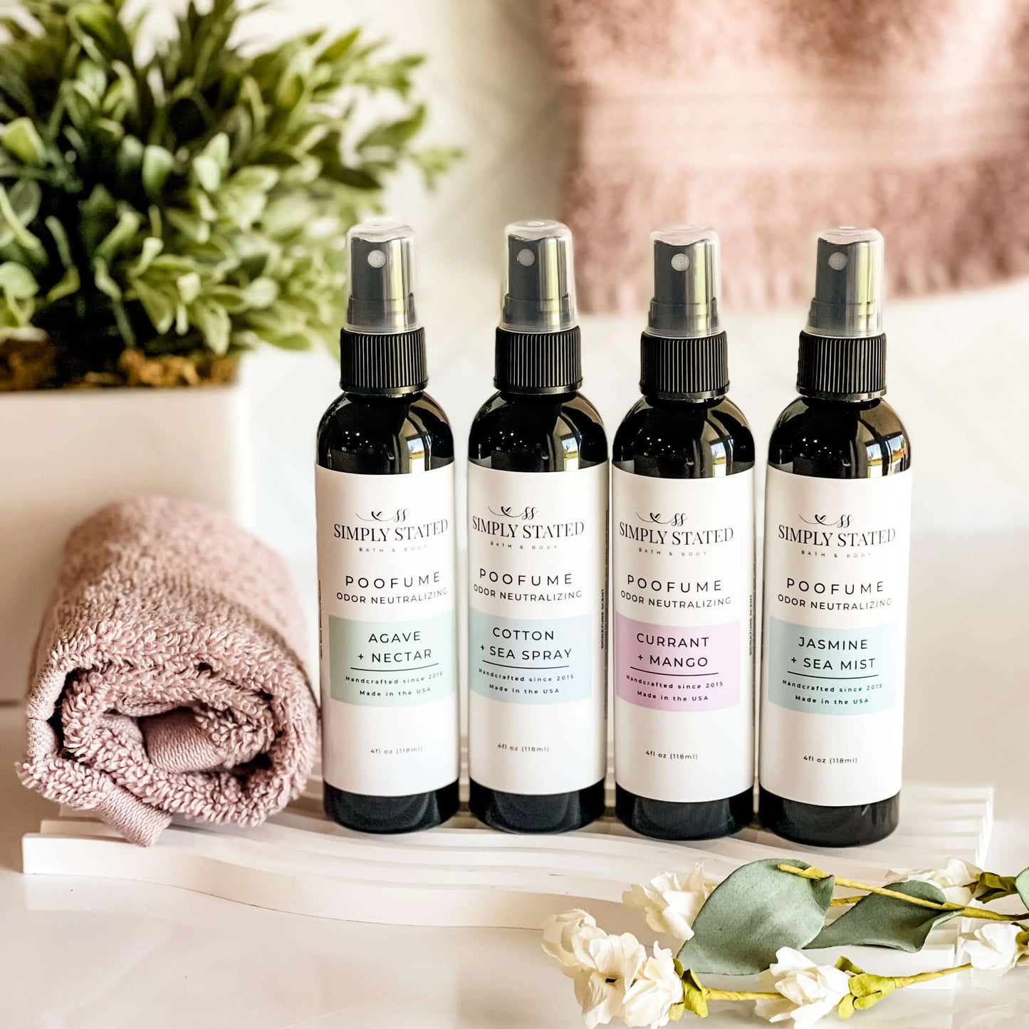 Four black spray bottles with white labels on a marble surface with a pink towel and flowers.