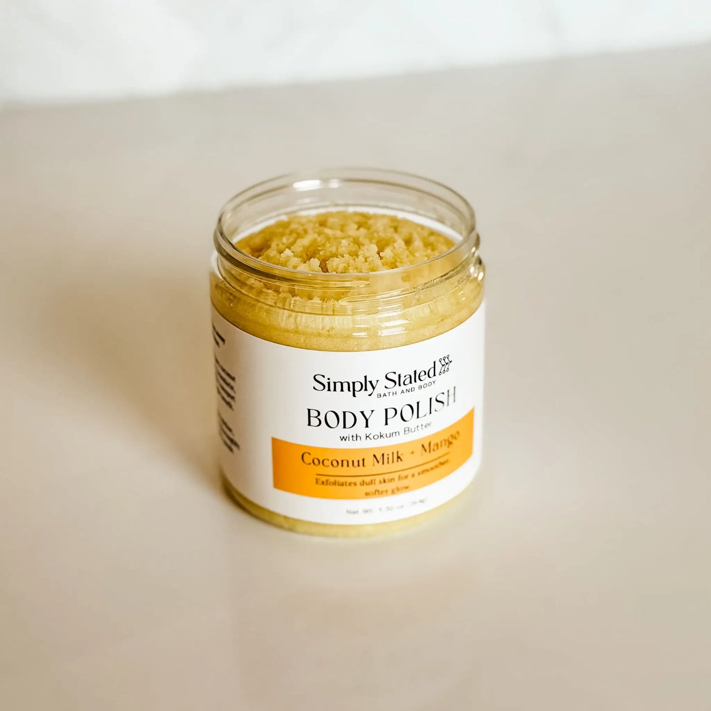 Simply Stated Bath and Body Coconut Milk + Mango Body Polish jar open, showing sugar scrub texture from above.