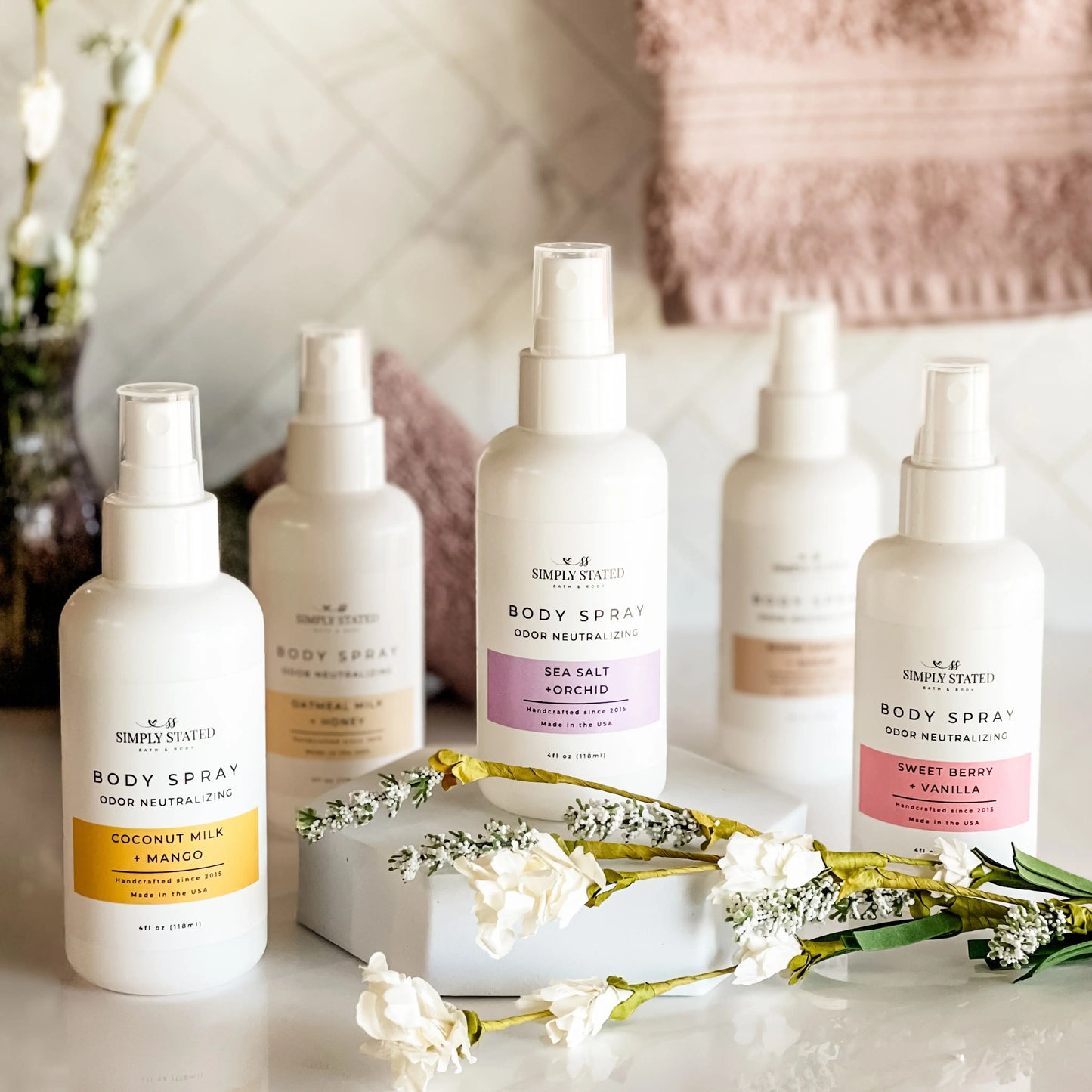 Simply Stated Bath and Body Coconut Milk + Mango Body Spray with four other scents lined up on tray with flowers.