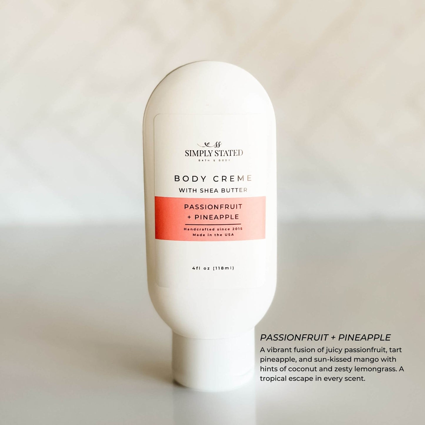 Simply Stated Passionfruit + Pineapple Body Crème in a white bottle with coral pink label, photographed against a neutral background with soft natural lighting.