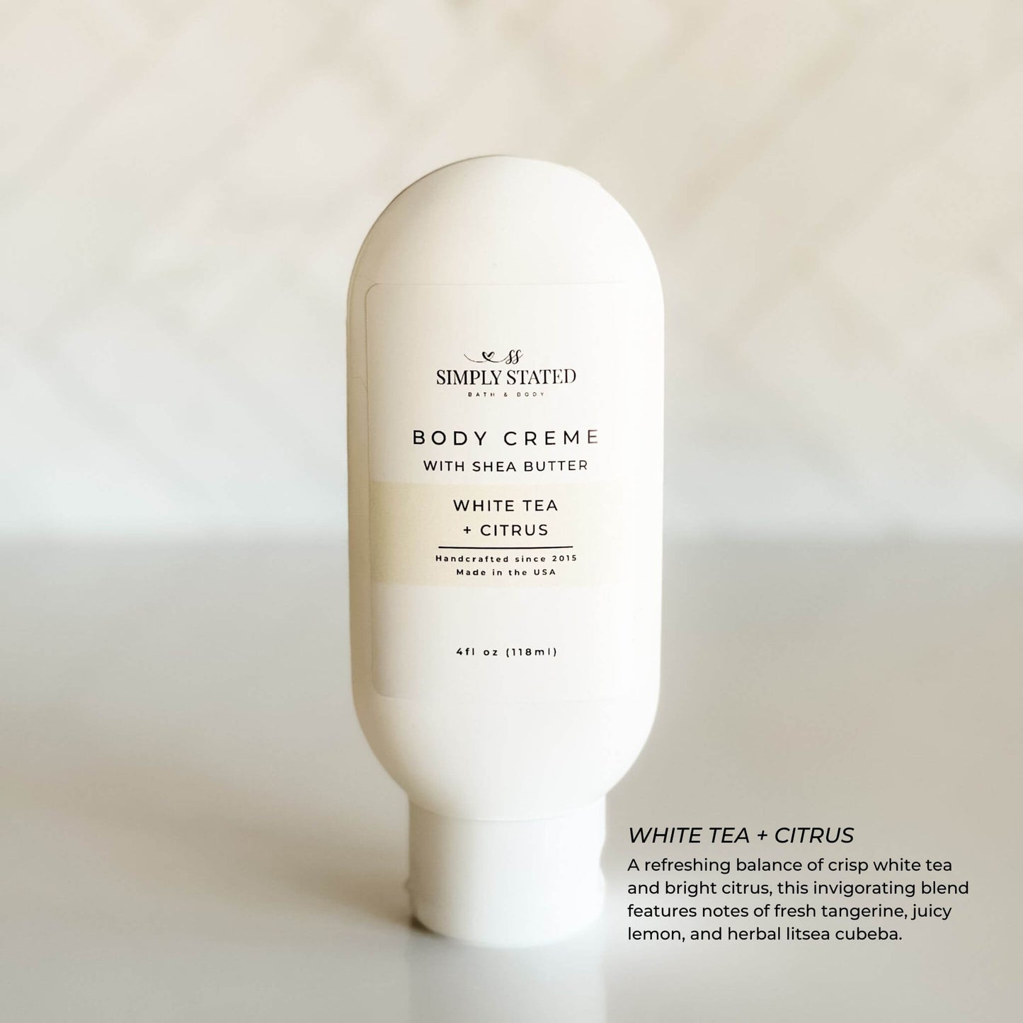 Simply Stated White Tea + Citrus Body Crème in an elegant white bottle with a light cream-colored label, highlighting its crisp, citrusy scent in a minimal lifestyle setting.