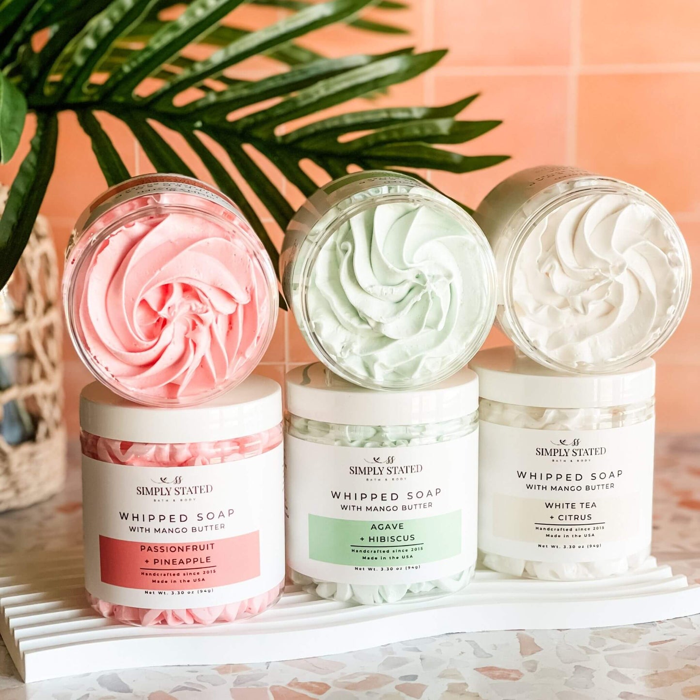 Summer Collection Whipped Soaps by Simply Stated – tropical scented trio of Agave + Hibiscus, Passionfruit + Pineapple, and White Tea + Citrus with swirl textures in open jars on terrazzo tile background.