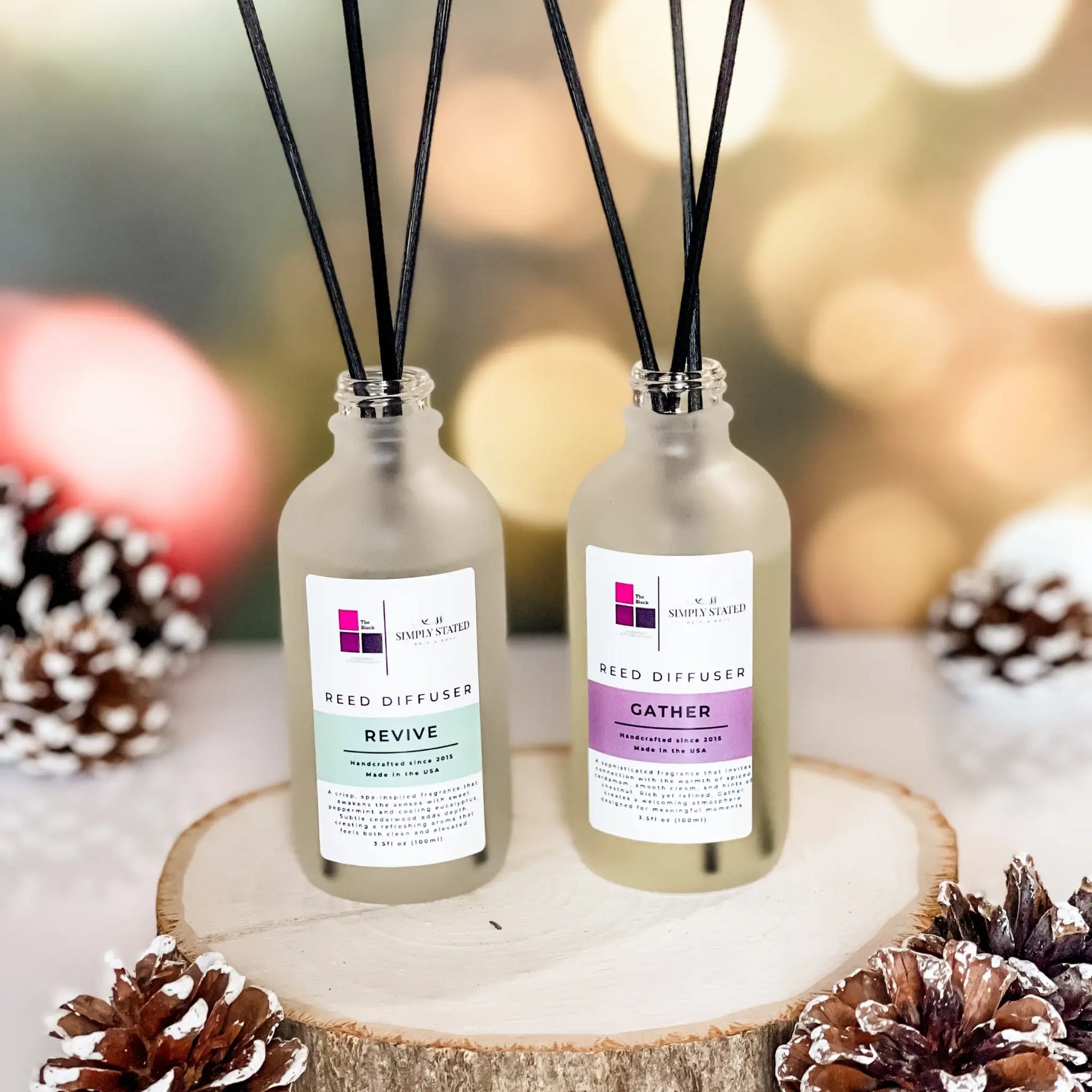 The Block x Simply Stated Reed Diffusers for rooms featuring scents in Revive and Gather with a warm winter glow background and pinecone decorations.