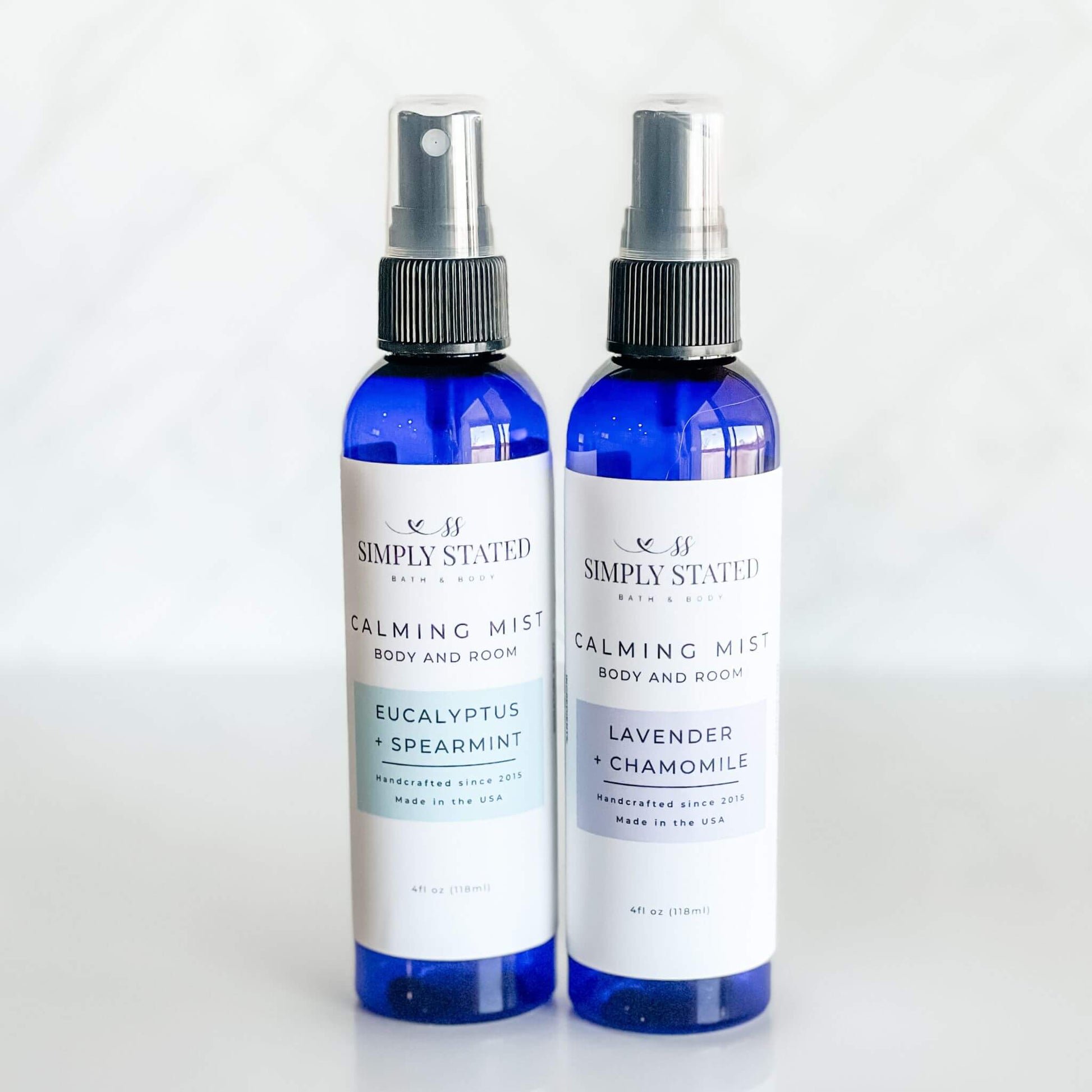 Simply Stated Bath & Body Calming Mist duo featuring Eucalyptus + Spearmint and Lavender + Chamomile. Body and room sprays crafted with essential oils to refresh, relax, and soothe. Presented in sleek 4oz blue bullet bottles.