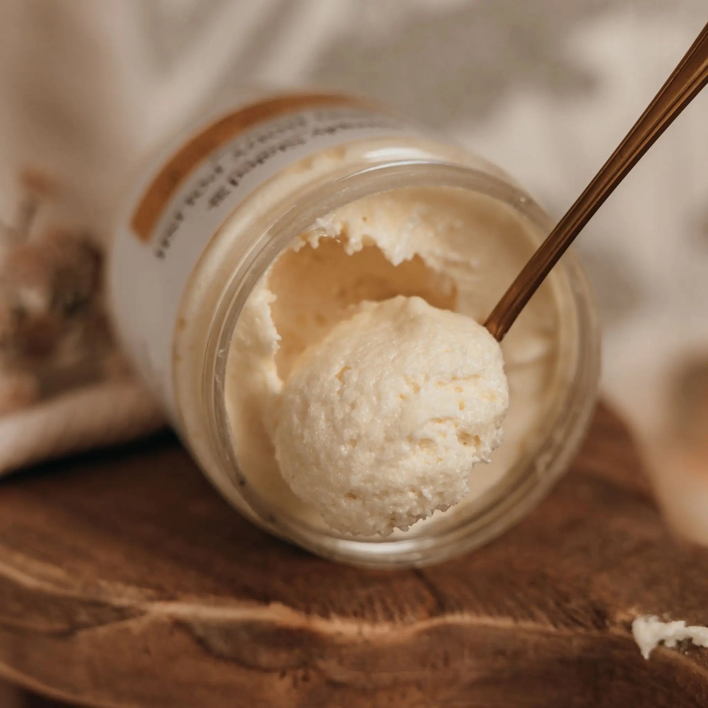 Whipped Body Butter jar open with spoon scooping creamy texture, on wooden surface.