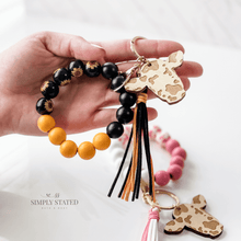 Bangle Keychain made with wood beads in solid black, solid yellow, and sunflower print. Wooden cow charm included.