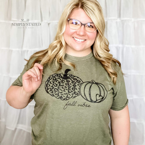 Graphic T-Shirt in Heather Olive with 2 pumpkins. One is pumpkin print and the other has a little heart in the bottom right hand half. The shirt says Fall Vibes