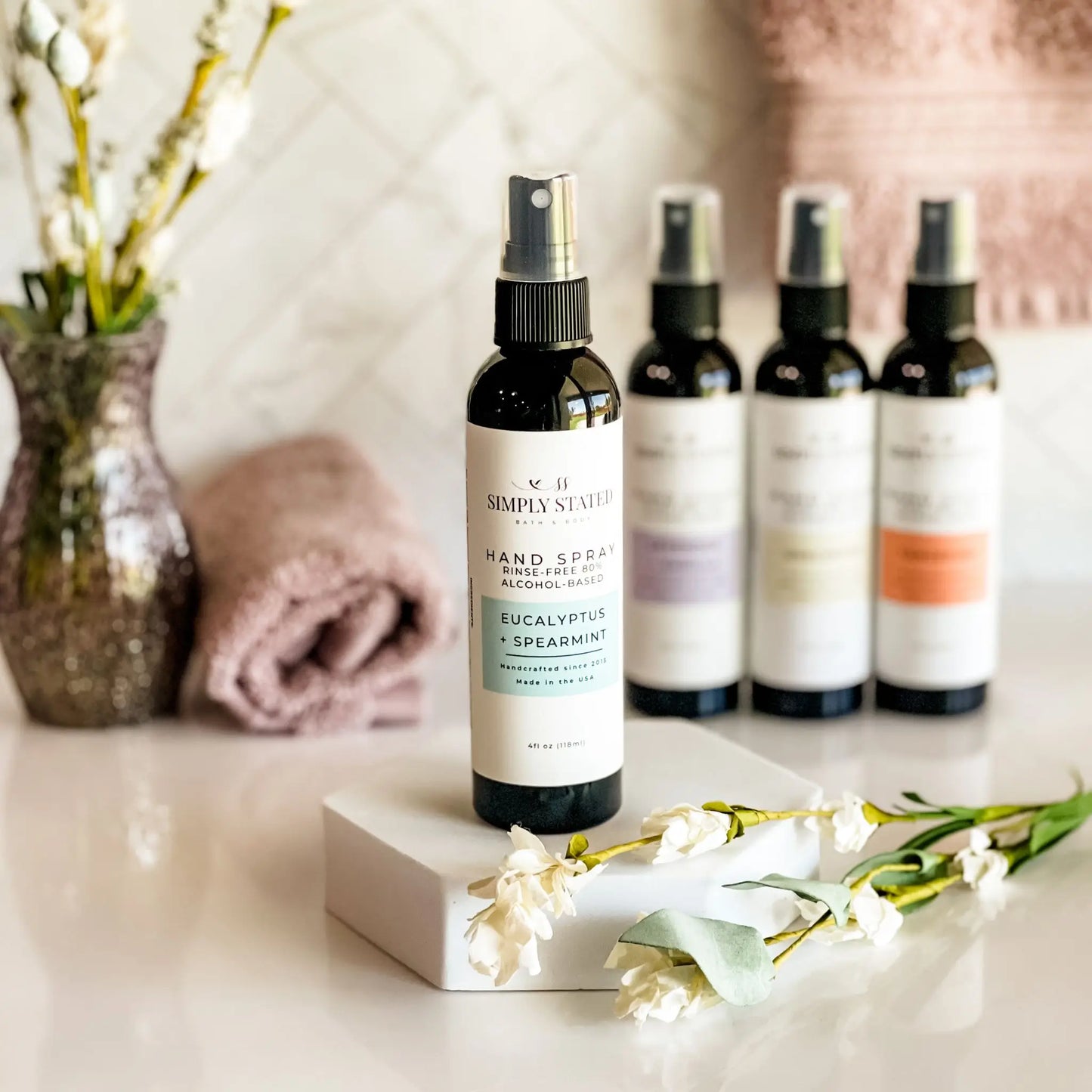 Hand sanitizer bottles with labels on a surface with flowers and towels in the background