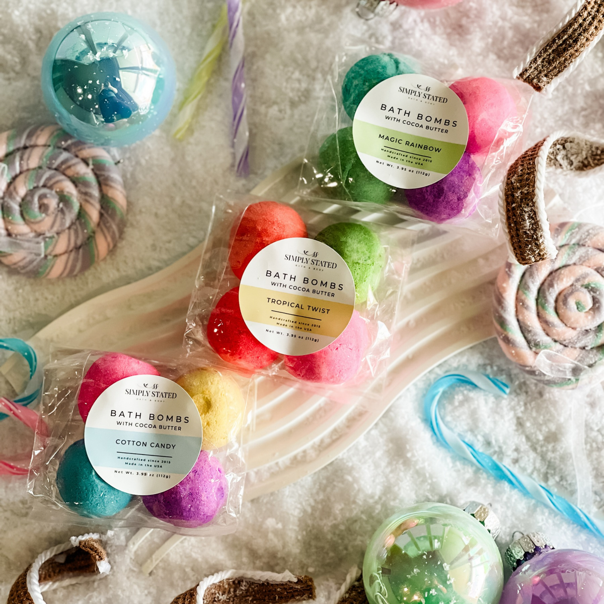 Simply Stated cocoa butter bath bombs in magic rainbow, tropical twist and cotton candy with candy canes and snow