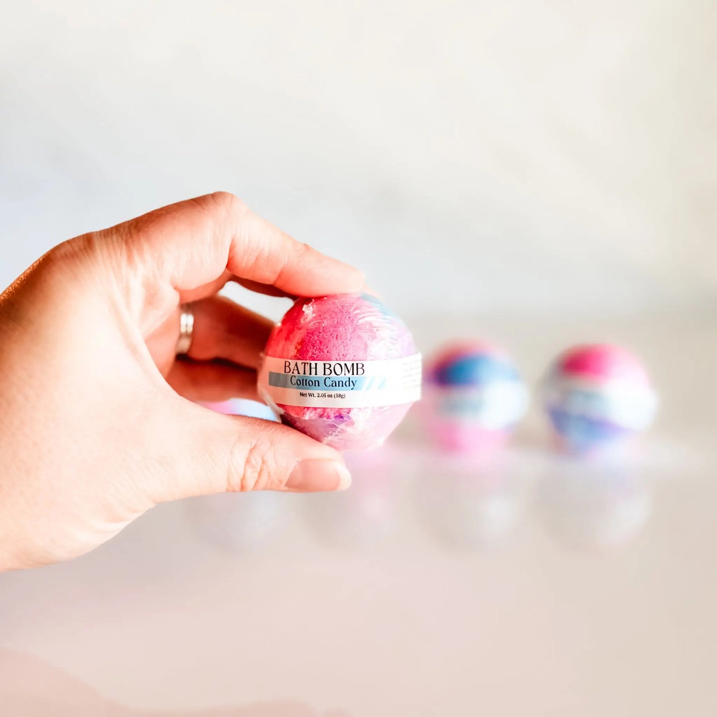 Bath Bomb in Cotton Candy, pink and blue swirled bath bomb held in hand with more bombs blurred in background