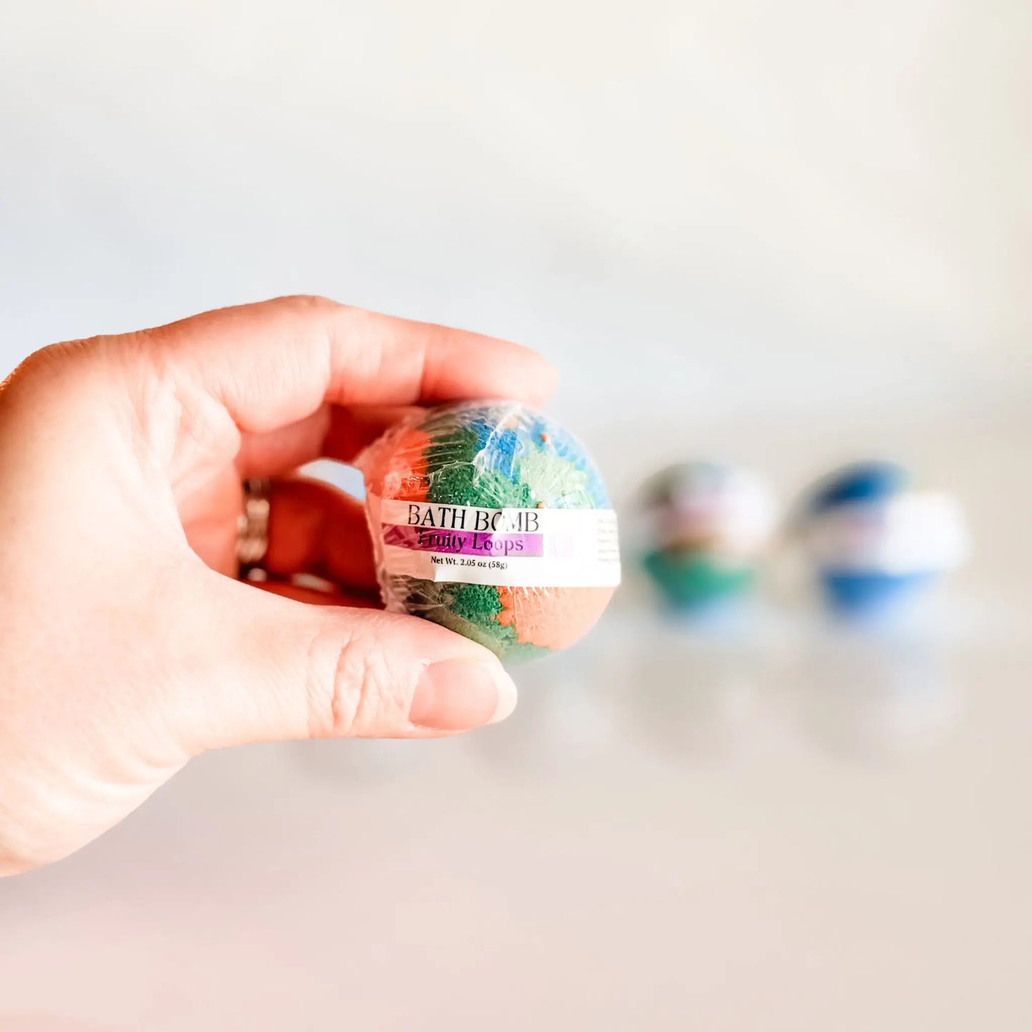 Bath Bomb in Fruity Loops, multicolor bath bomb held in hand with more bombs blurred in background
