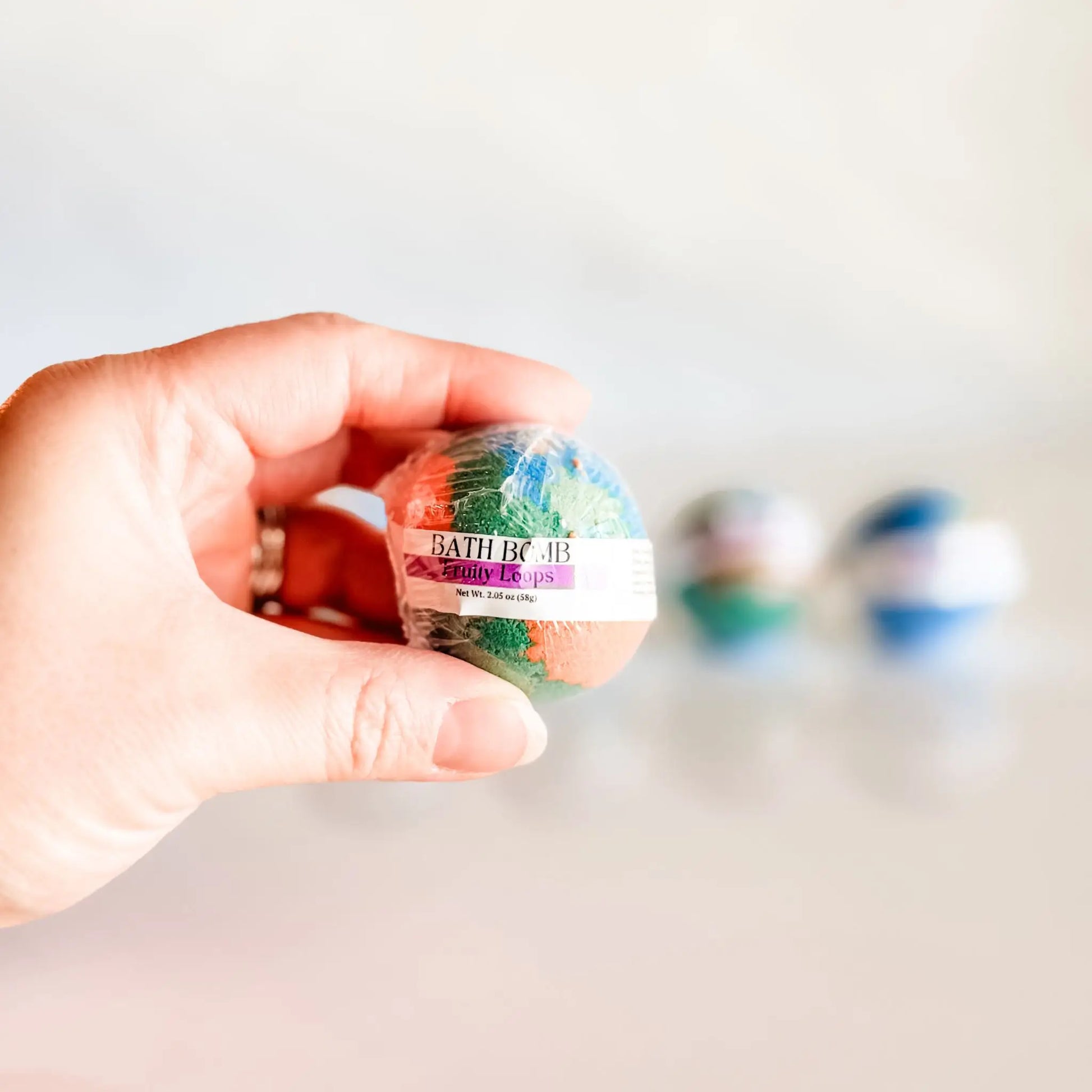 Bath Bomb in Fruity Loops, multicolor bath bomb held in hand with more bombs blurred in background