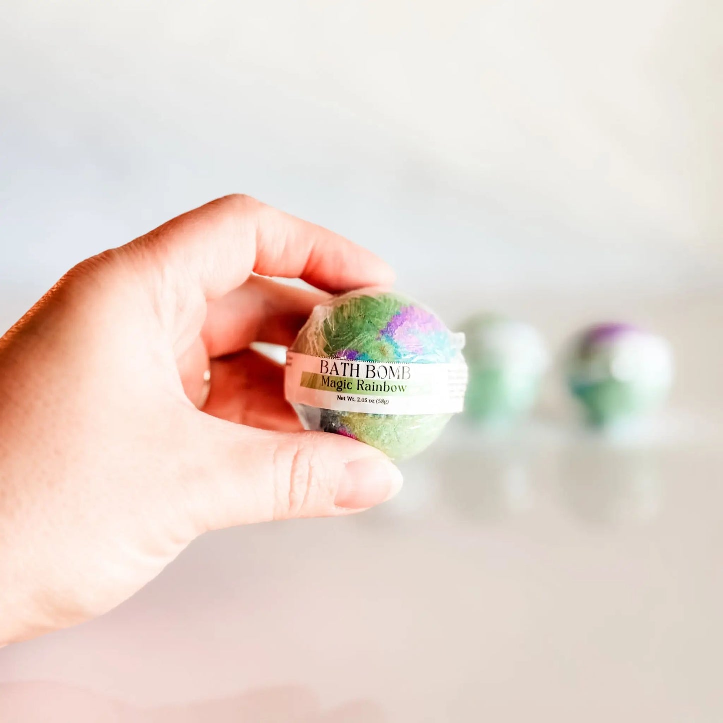 Bath Bomb in Magic Rainbow, green and purple bath bomb held in hand with more bombs blurred in background