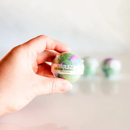 Bath Bomb in Magic Rainbow, green and purple bath bomb held in hand with more bombs blurred in background