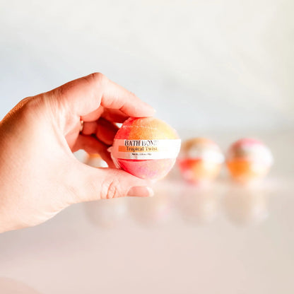 Bath Bomb in Tropical Twist, orange and pink bath bomb held in hand with more bombs blurred in background