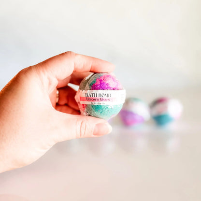 Bath Bomb in Unicorn Kisses, teal and pink bath bomb held in hand with more bombs blurred in background