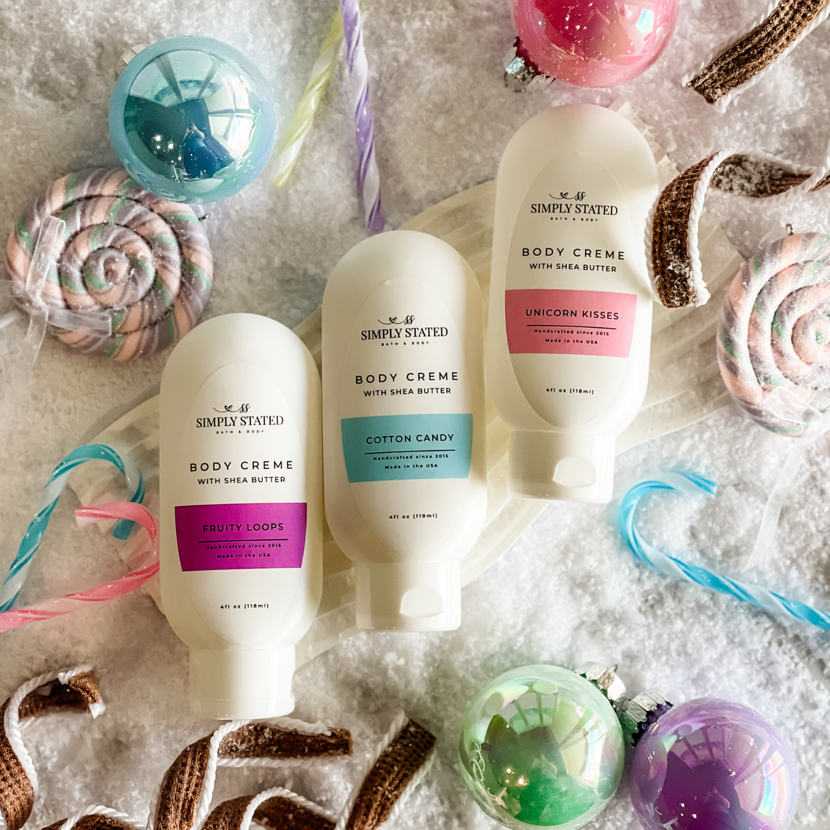 Fruity Loops, Cotton Candy, and Unicorn Kisses body cremes with shea butter in colorful candy-themed setting.