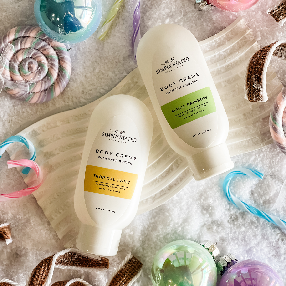 Simply Stated Tropical Twist and Magic Rainbow Body Creme with shea butter, flat lay with candy canes and ornaments.