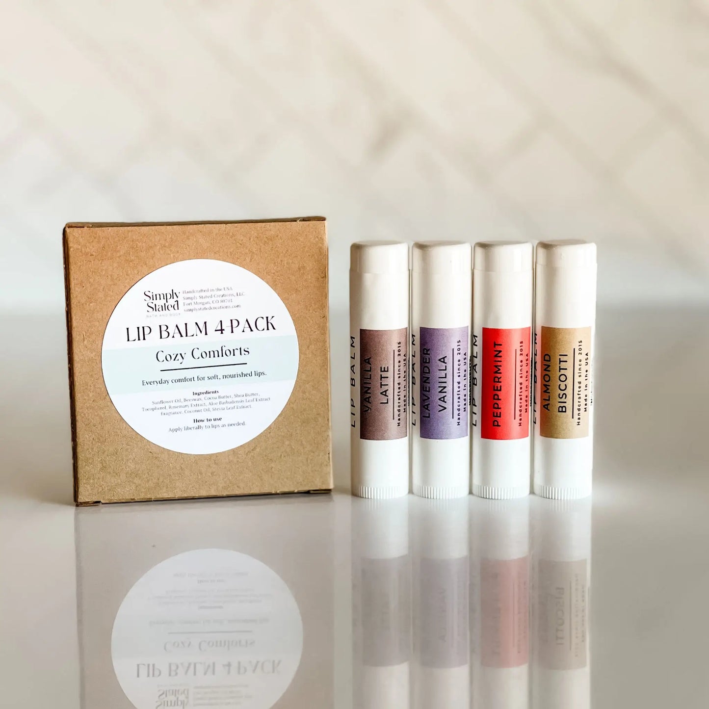 Lip balm 4-pack with a cardboard box labeled 'Cozy Comforts' on a reflective surface.