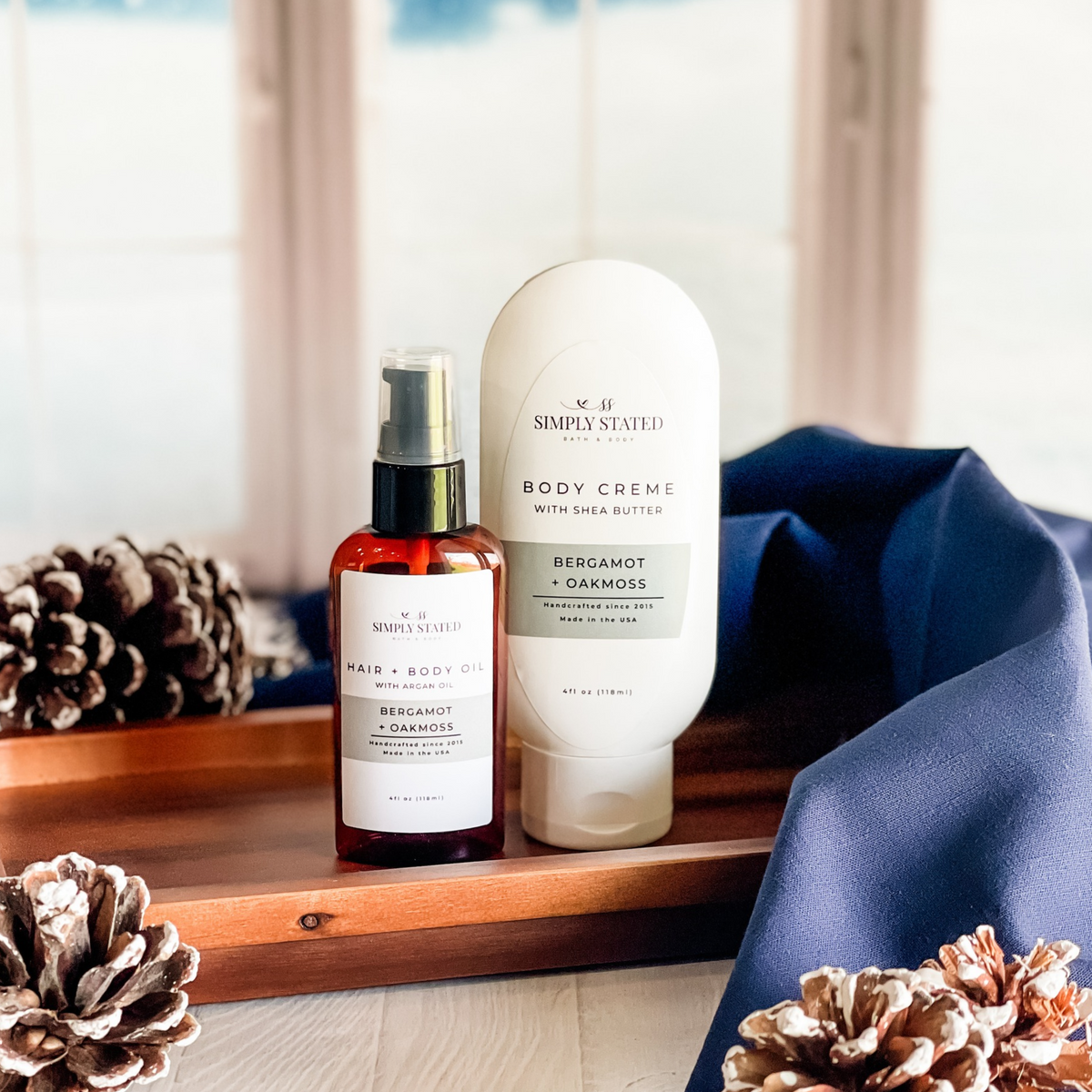 Simply Stated bergamot oakmoss hair and body oil with argan oil and shea butter body creme beside pinecones