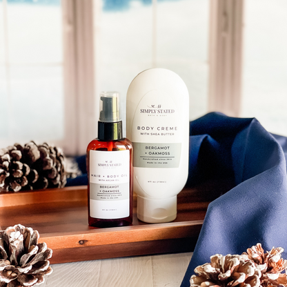Simply Stated bergamot oakmoss hair and body oil with argan oil and shea butter body creme beside pinecones
