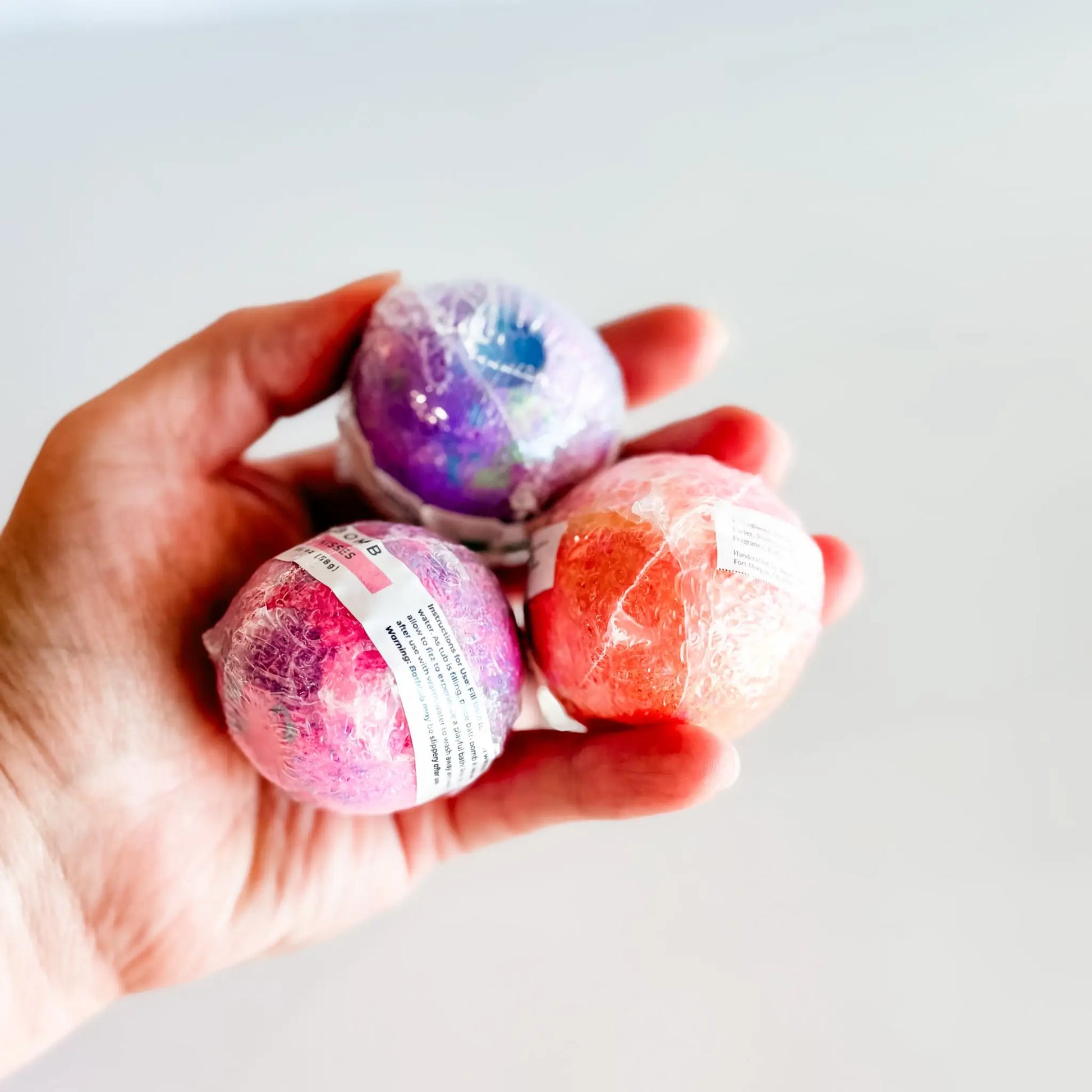 Hand holding three colorful bath bombs against a light background