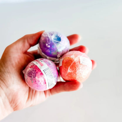 Hand holding three colorful bath bombs against a light background
