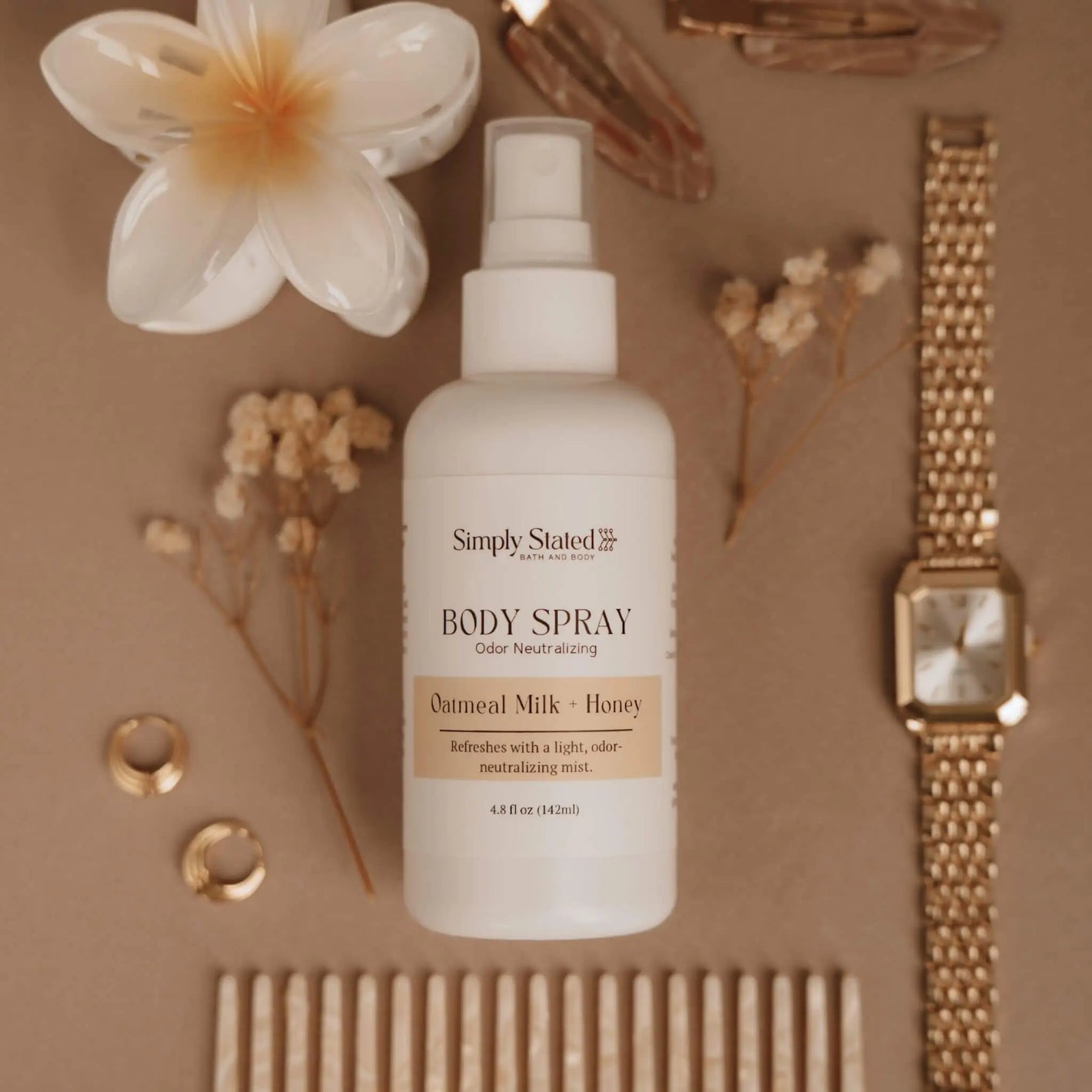Simply Stated Bath and Body Oatmeal Milk + Honey Body Spray bottle styled with flowers, jewelry, and comb.