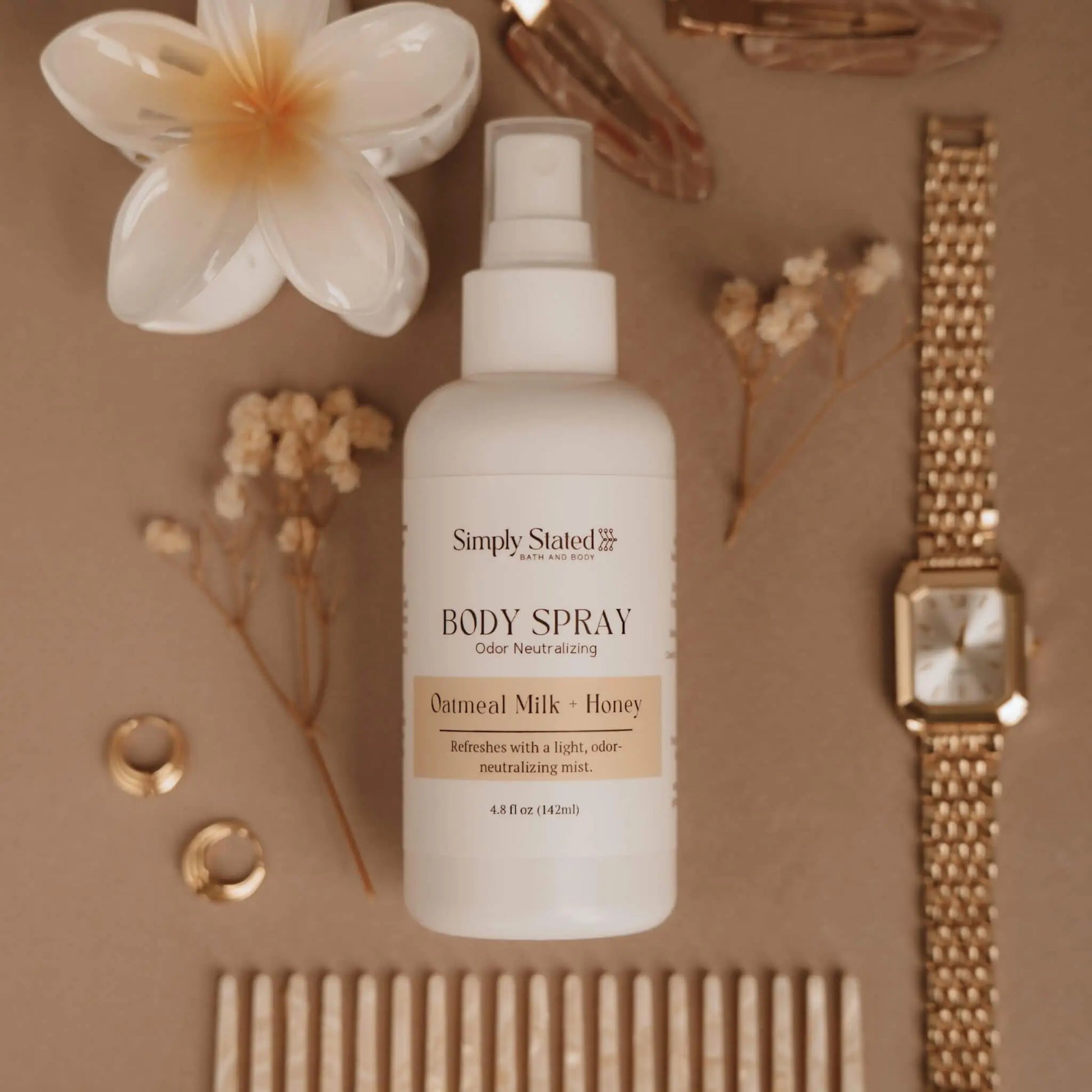 Simply Stated Bath and Body Oatmeal Milk + Honey Body Spray bottle styled with flowers, jewelry, and comb.