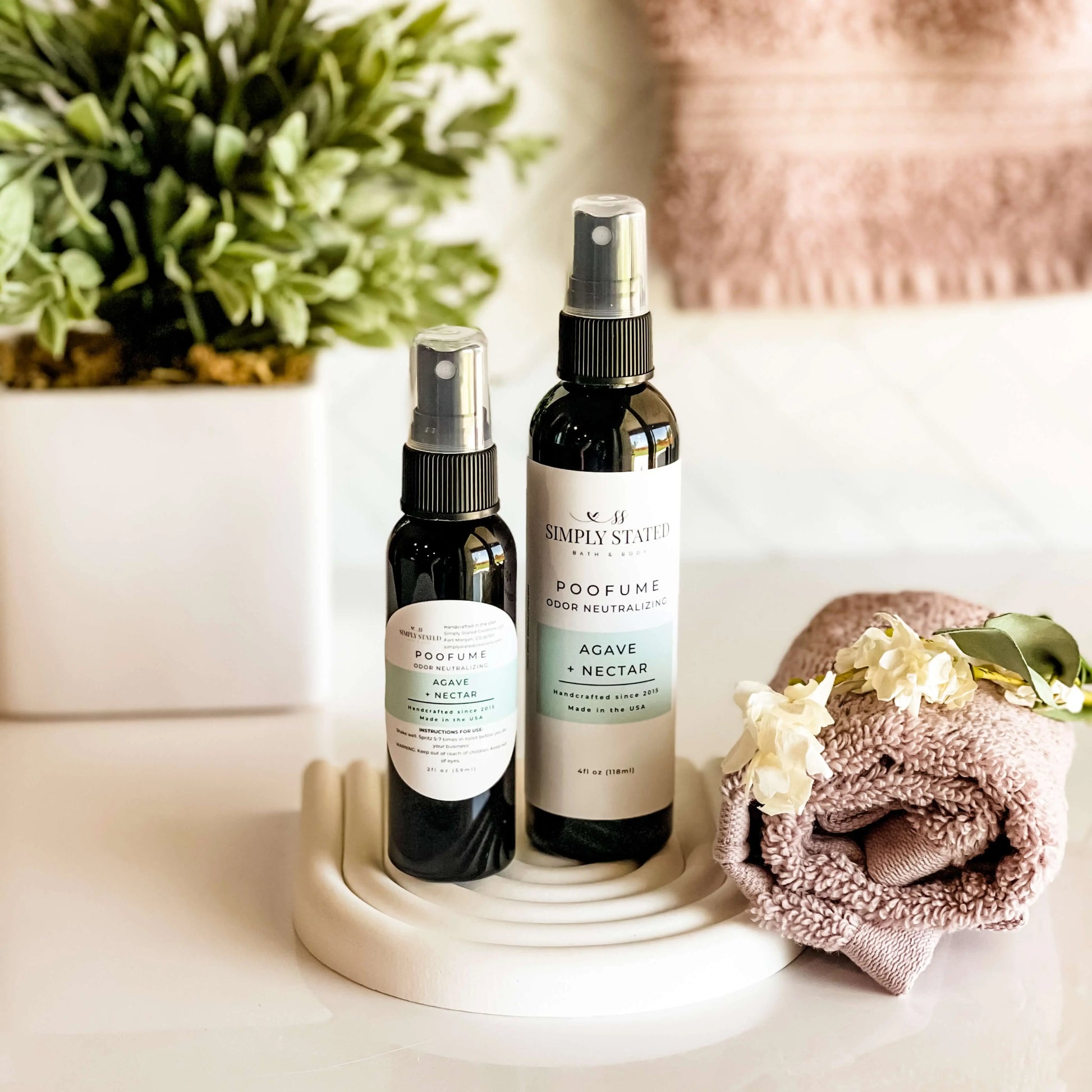 Two spray bottles on a white surface with a plant and towel in the background