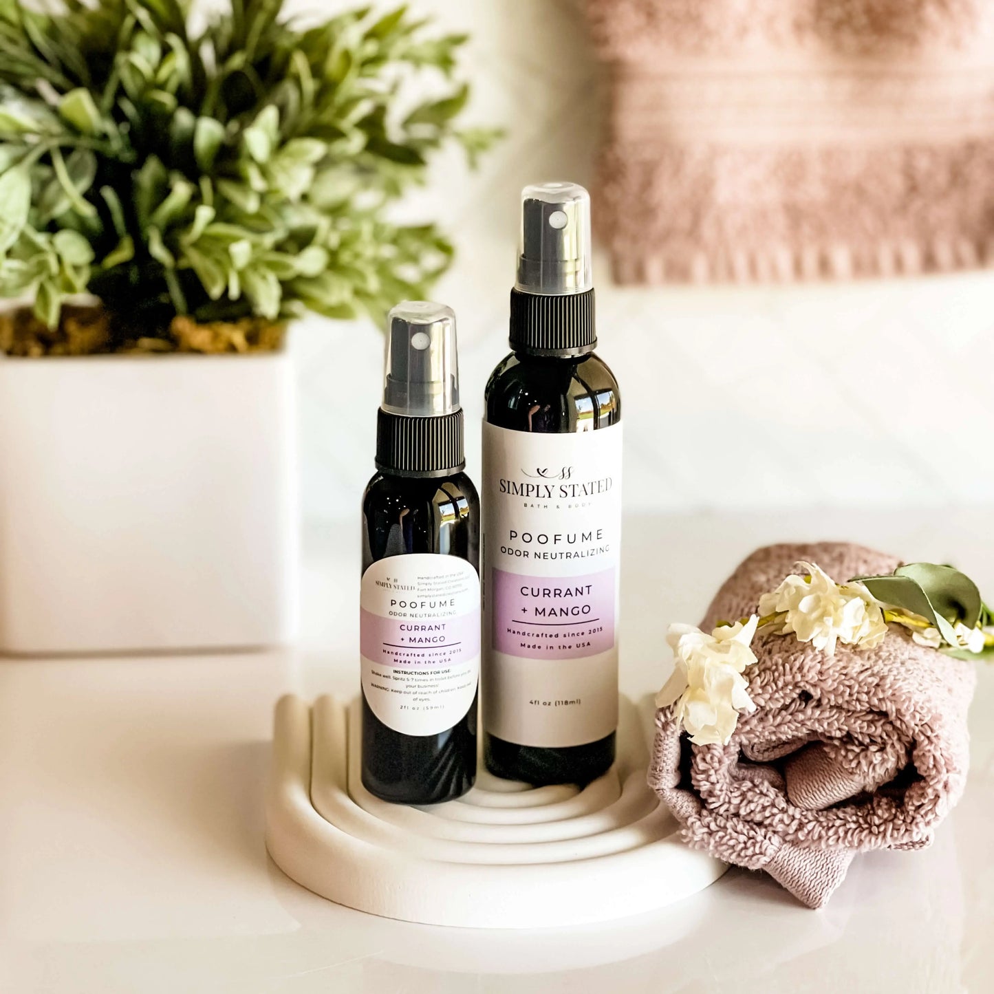 Two spray bottles on a white surface with a plant and towel in the background