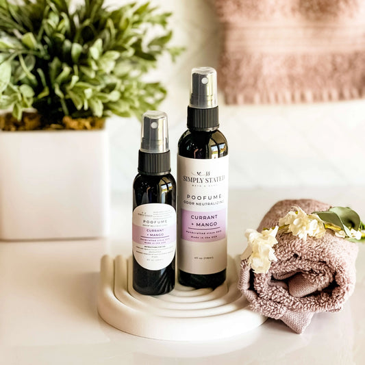 Two spray bottles on a white surface with a plant and towel in the background