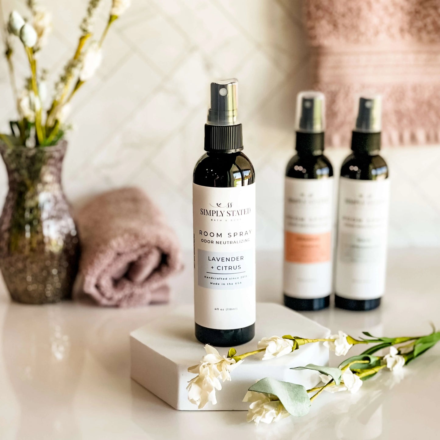 Room spray bottles on a surface with flowers and towels in the background