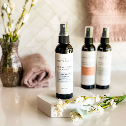 Room spray bottles on a surface with flowers and towels in the background