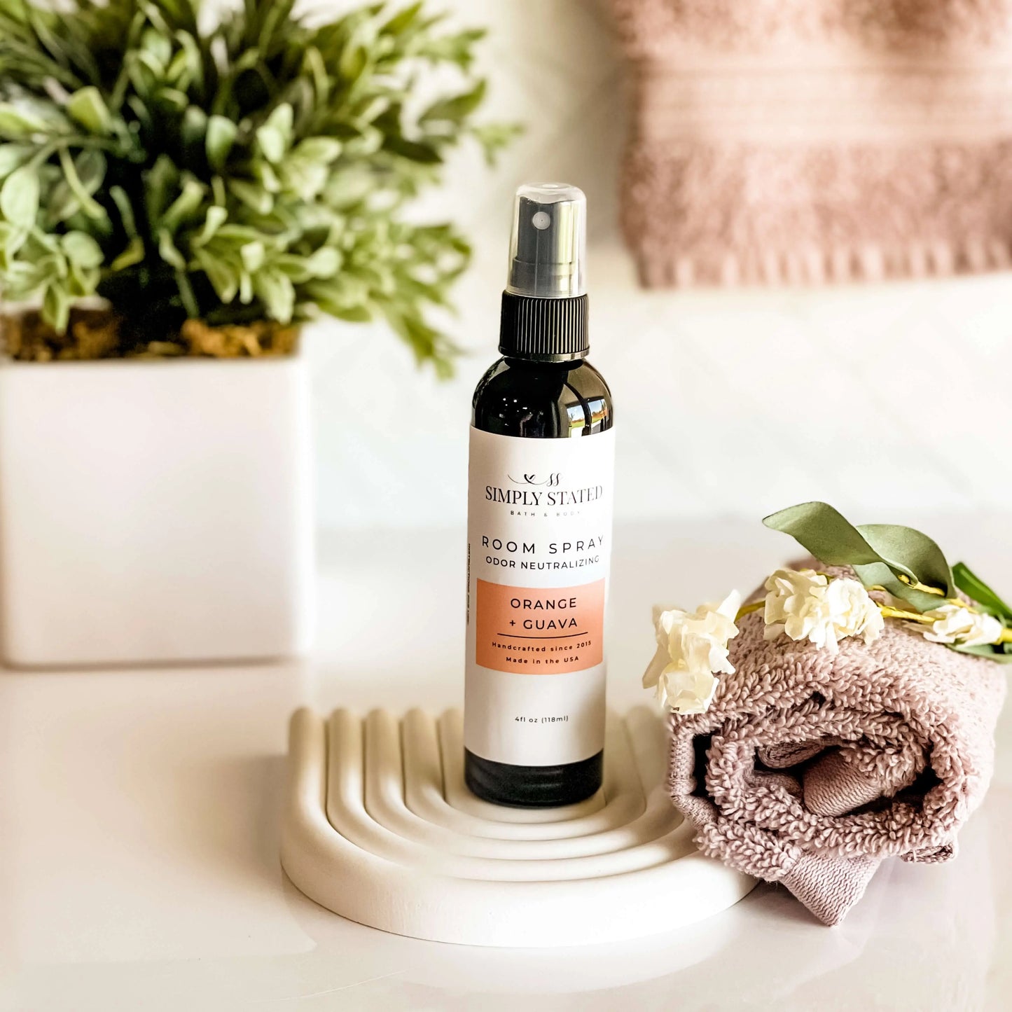 Room spray bottle on a decorative stand with flowers and a plant in the background