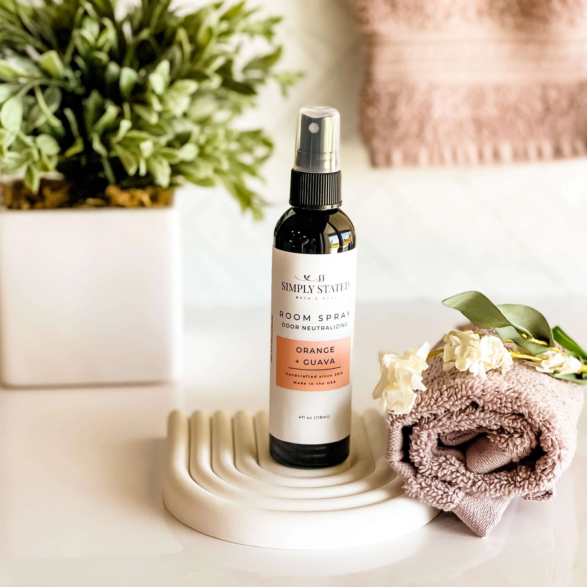 Room spray bottle on a decorative stand with flowers and a plant in the background