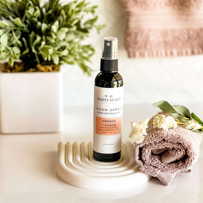 Room spray bottle on a decorative stand with flowers and a plant in the background
