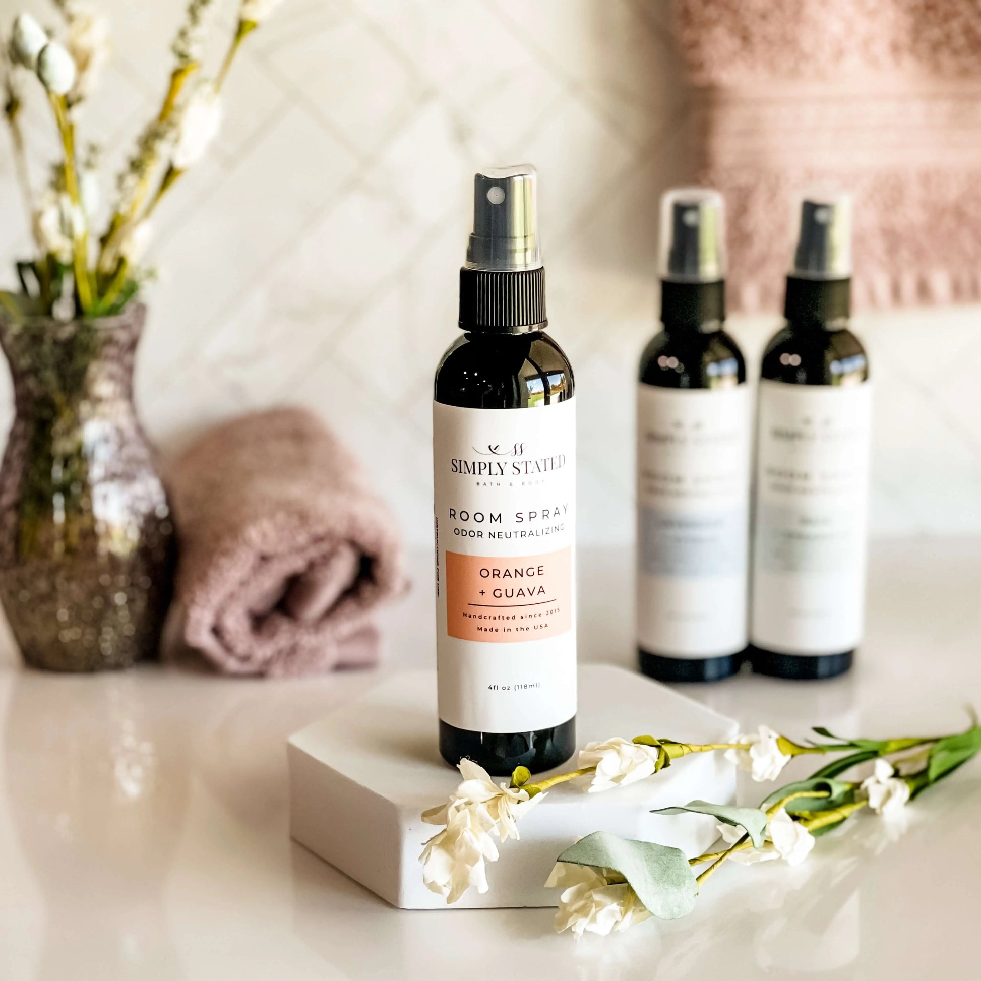 Room spray bottle with flowers and towels in the background