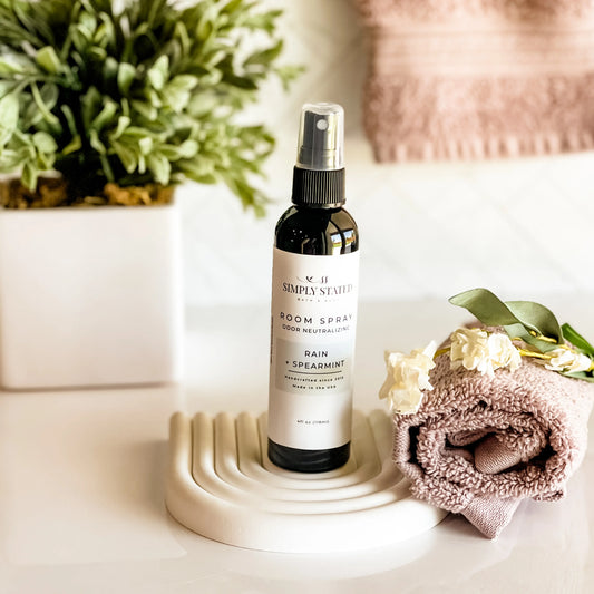 Room spray bottle on a decorative stand with flowers and a plant in the background