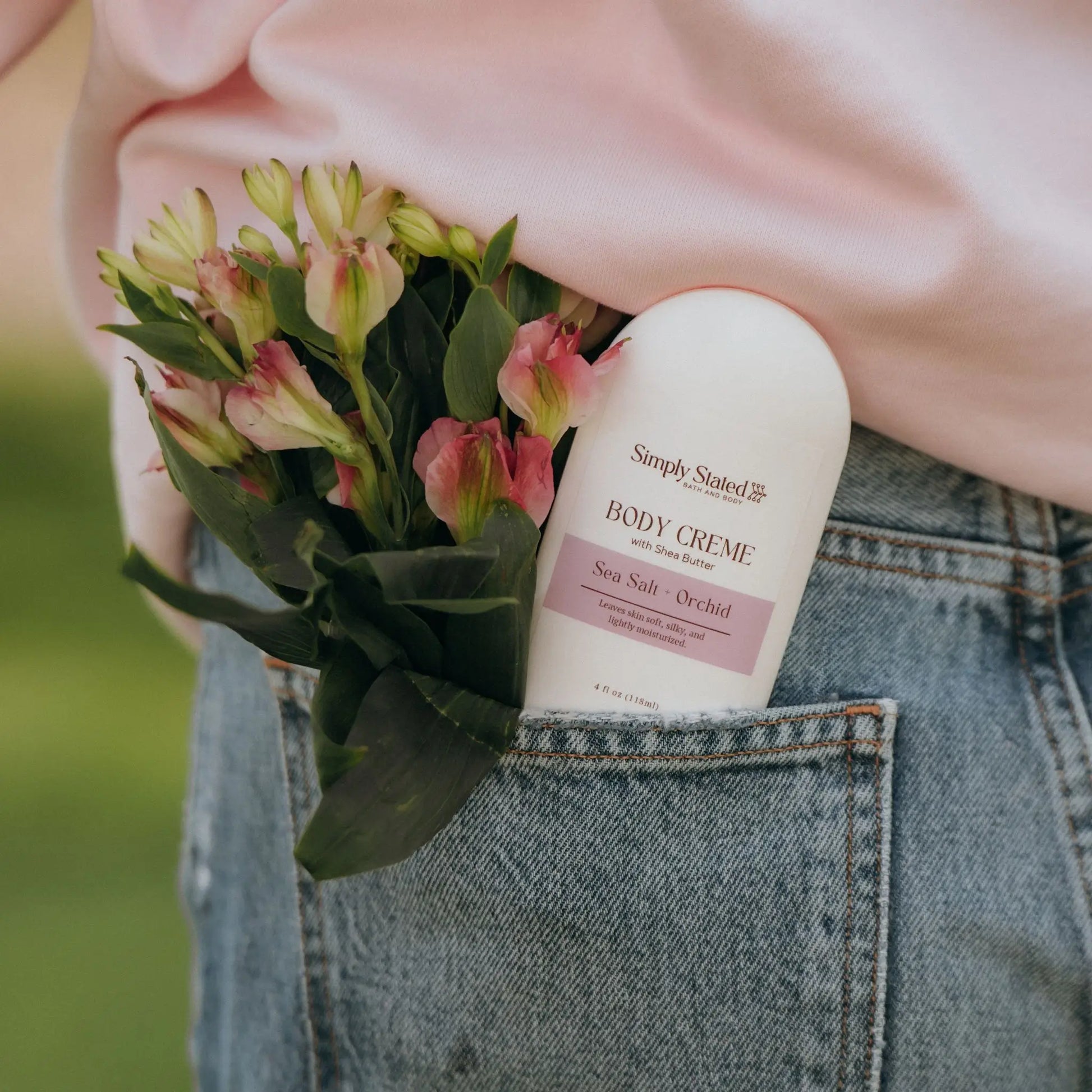 Sea Salt + Orchid Body Creme bottle tucked in denim jean pocket with pink flowers
