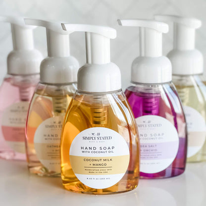 A vibrant collection of Simply Stated Bath & Body Signature Hand Soaps in 8oz foaming pump bottles, featuring fragrances like Coconut Milk + Mango, Oatmeal Milk + Honey, Sea Salt + Orchid, Sweet Berry + Vanilla, and Warm Vanilla + Sugar.