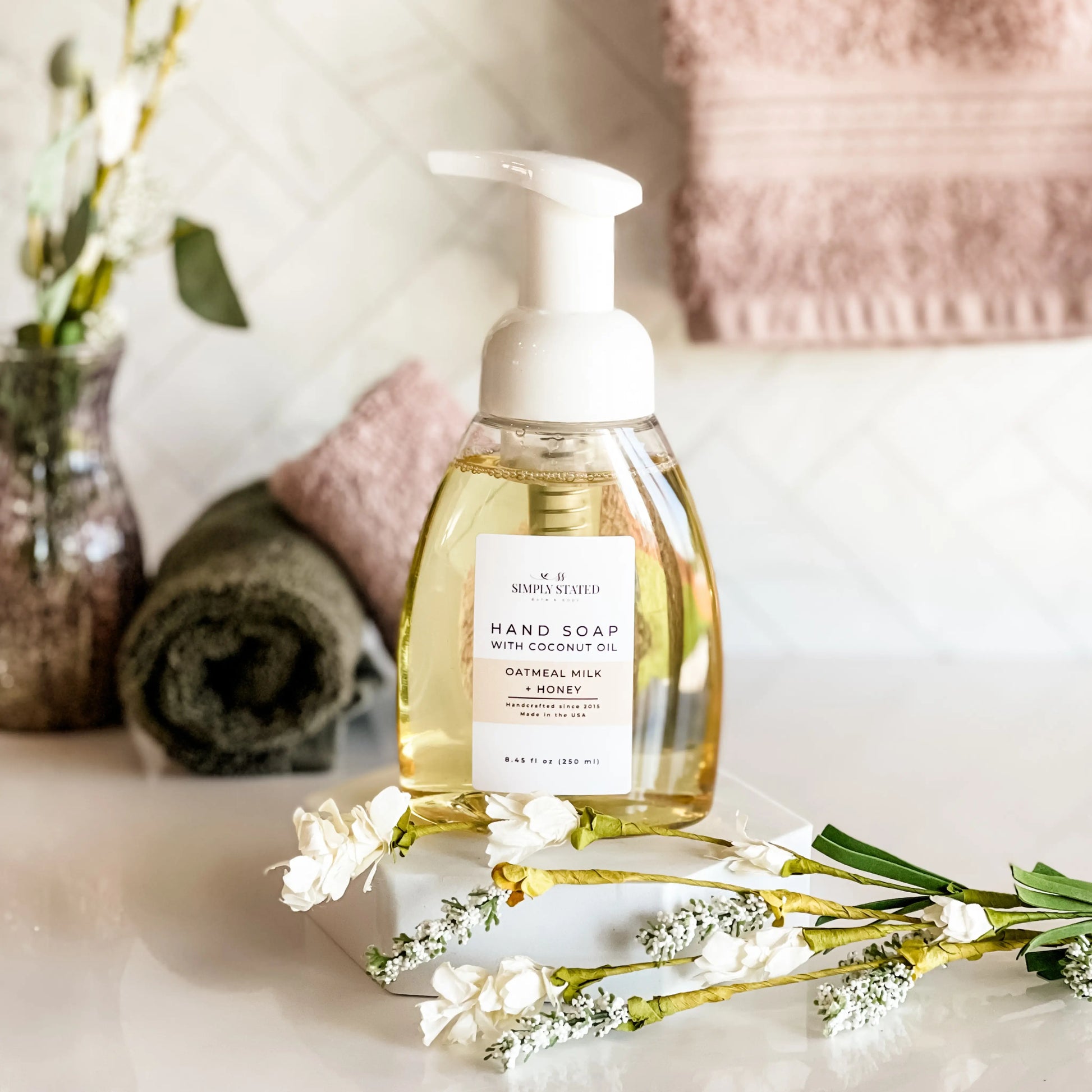 Hand soap bottle with pump on a marble surface with flowers and towels in the background
