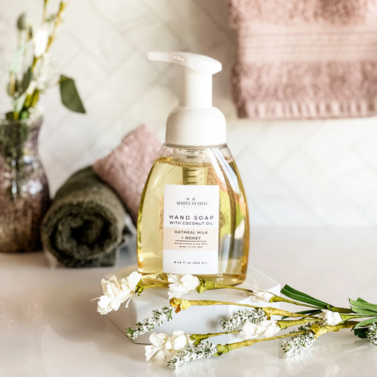 Hand soap bottle with pump on a marble surface with flowers and towels in the background