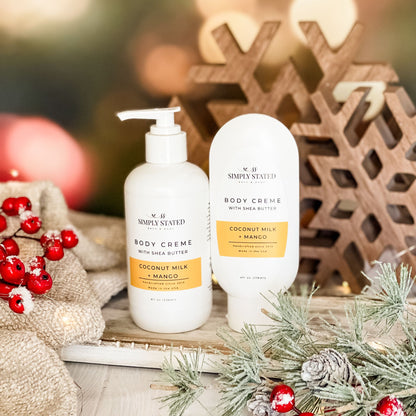 Simply Stated Coconut Milk + Mango Body Creme with shea butter, pump and tube sizes, with wooden snowflakes and berries.