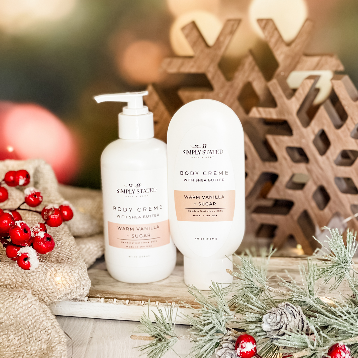 Simply Stated Warm Vanilla + Sugar Body Creme with shea butter, pump and tube sizes, with wooden snowflakes and berries.