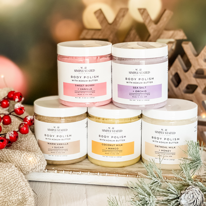 Simply Stated Body Polish collection with kokum butter, five scents stacked beside wooden snowflakes and red berries.