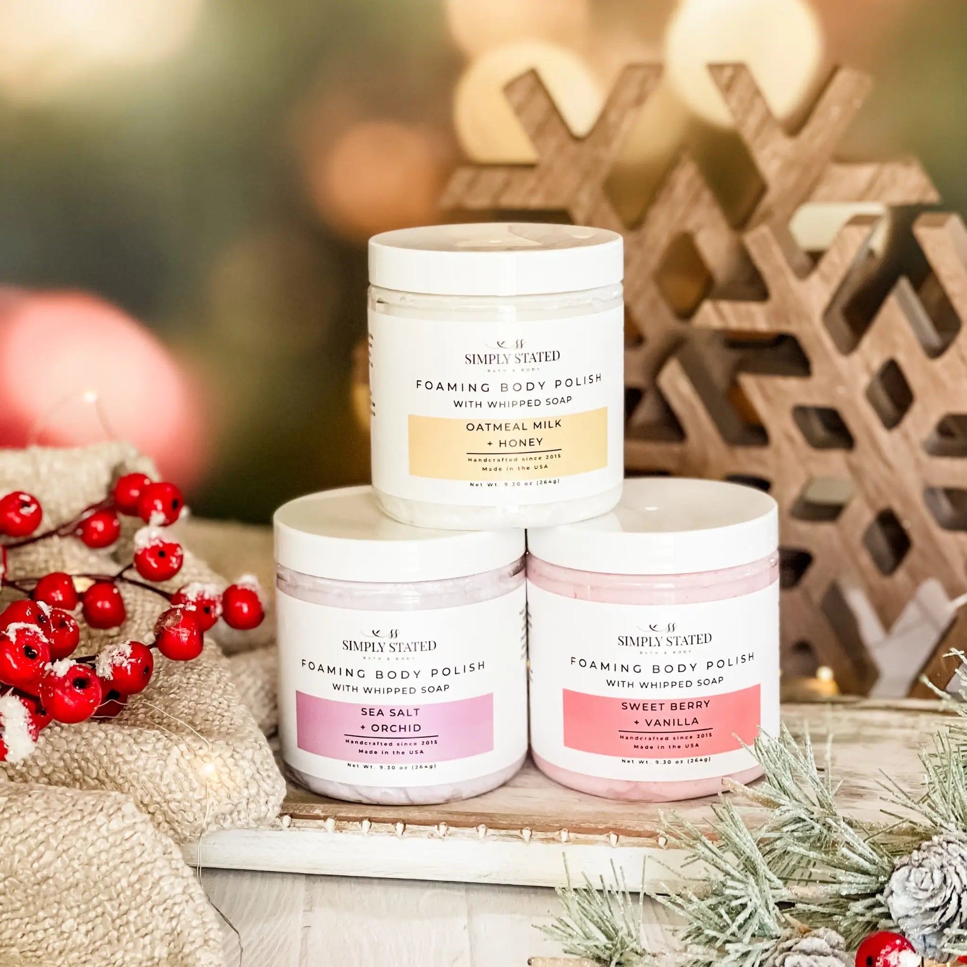 Three jars of Simply Stated foaming body polish on a decorative surface with Christmas decorations.